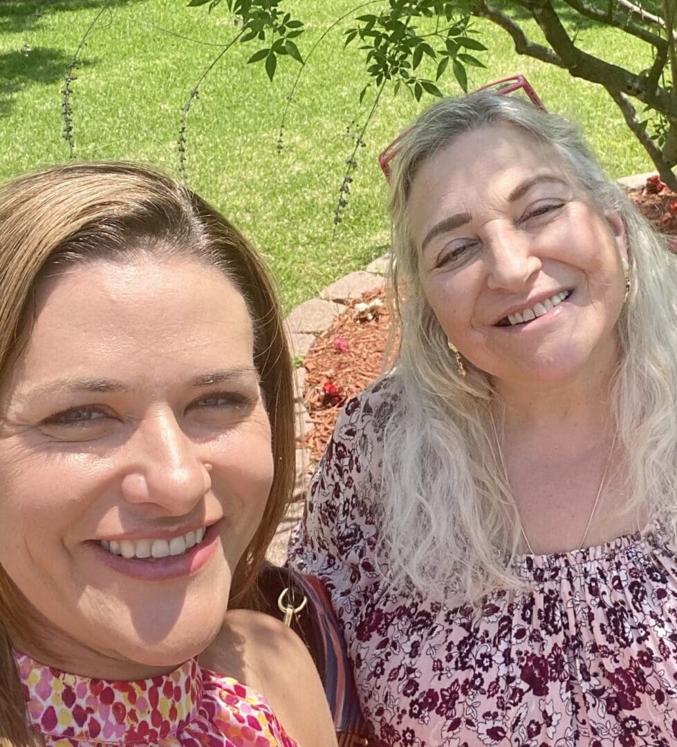 Two women smiling for a picture while sitting on the ground.